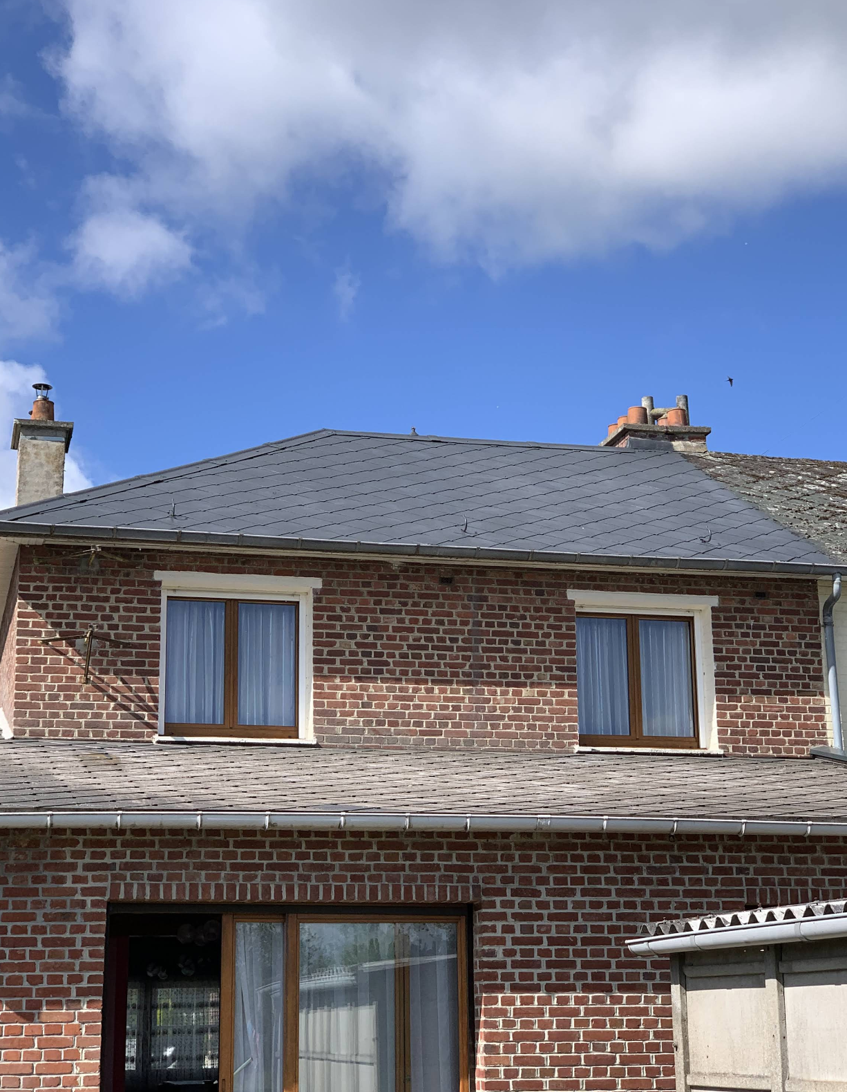 Toiture en ardoises rénovée sur maison en briques avec cheminées